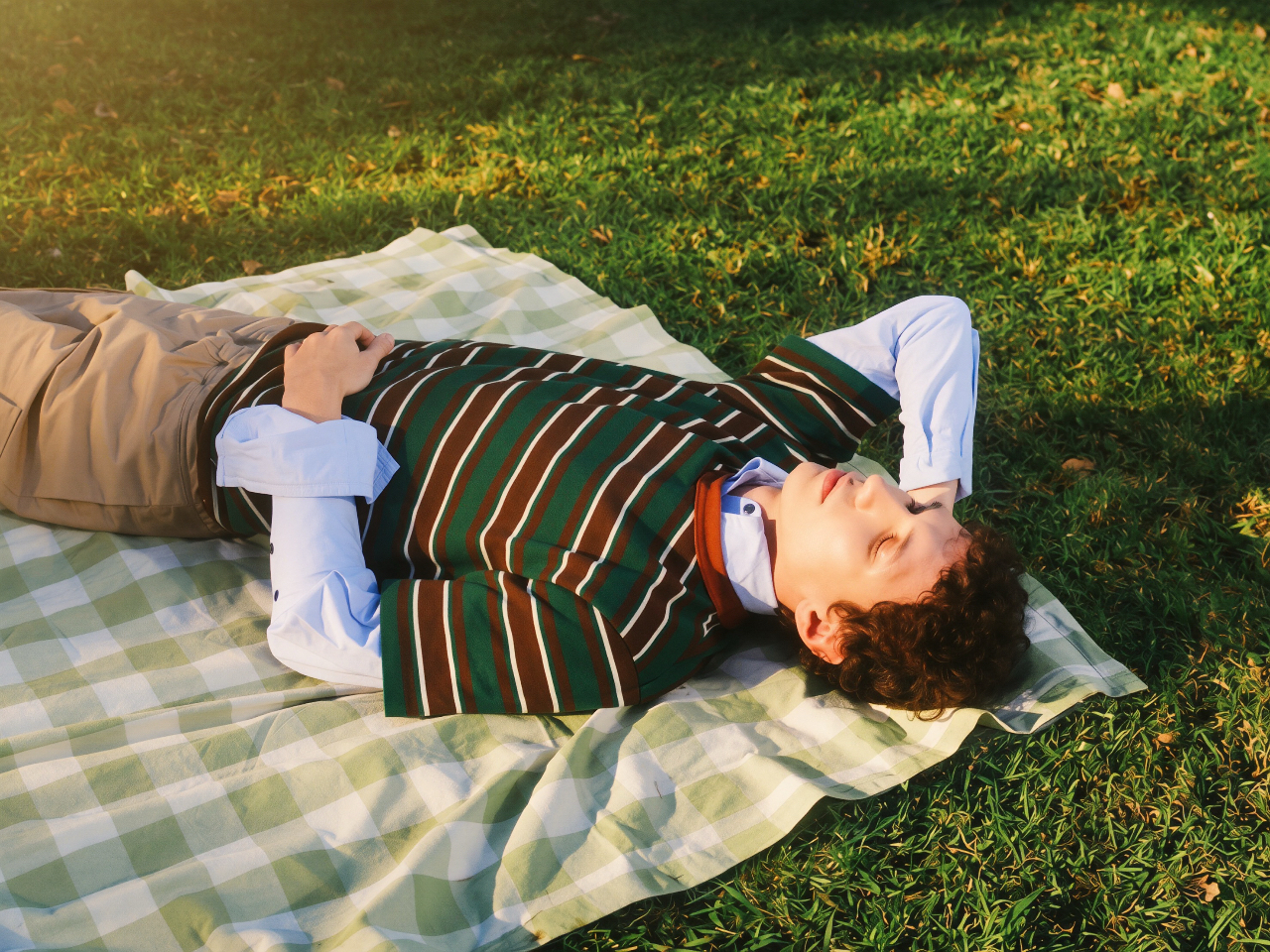 A young man resting on a picnic blanket in the sun, eyes closed