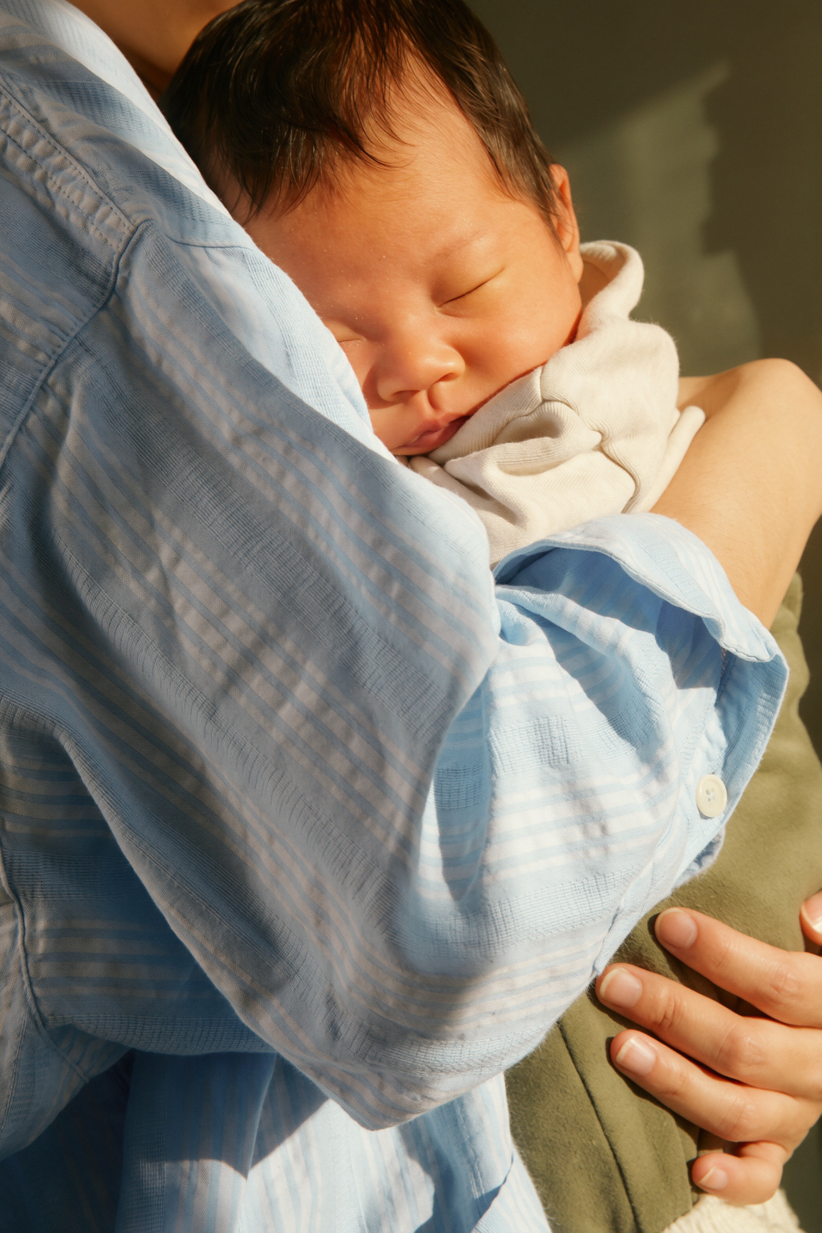 A newborn asleep on a parent's shoulder in the sun