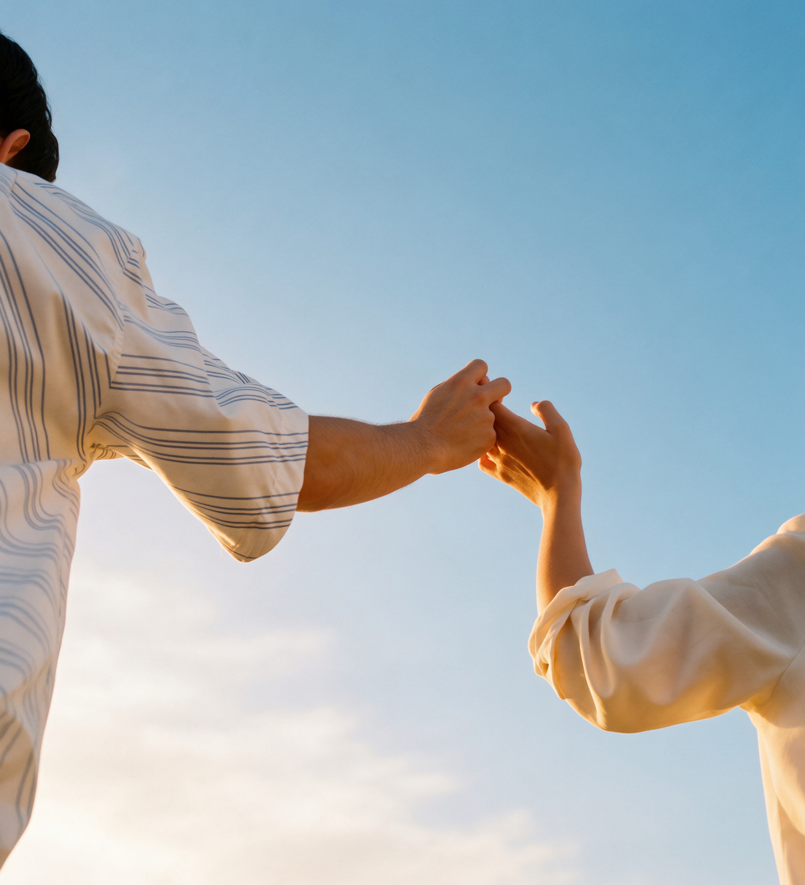 Two hands reaching for each other against a blue sky