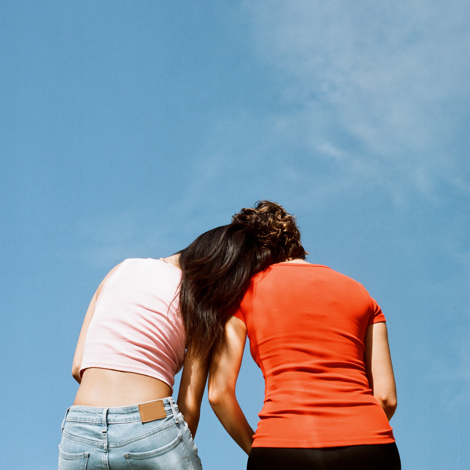 Two friends leaning their heads together under a blue sky