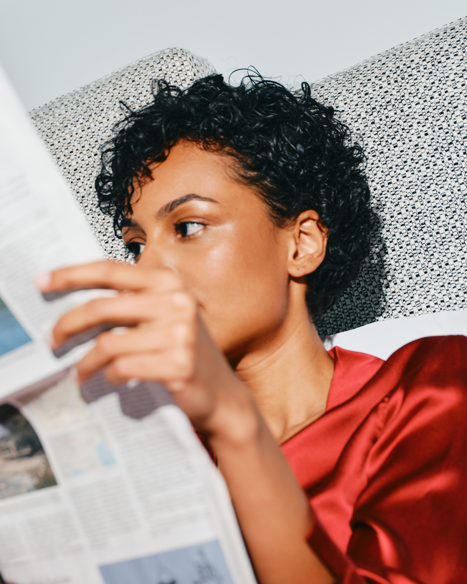 A woman in red satin reading a newspaper, glancing over the page