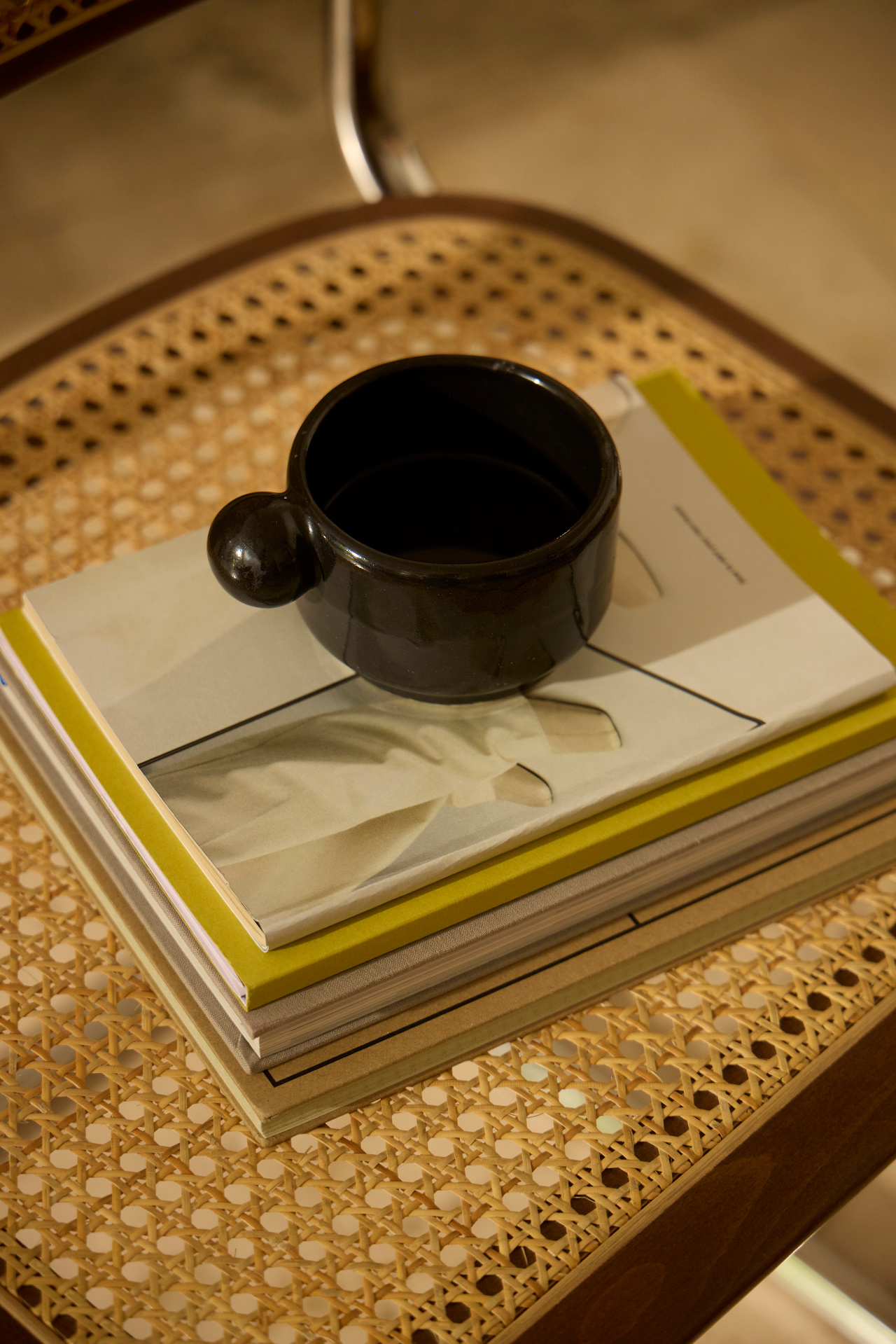 A black cup on a pile of books on a cane chair